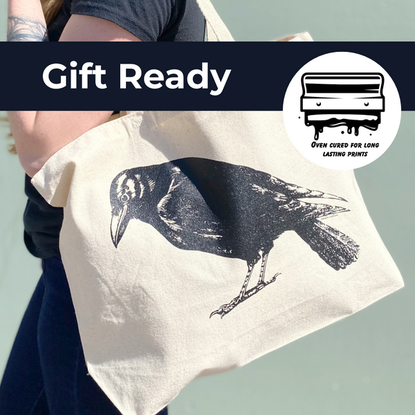 A person is holding a white tote bag with a black and white illustration of a bird on it.