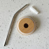 Top view of bamboo lid, stainless steel straw, and silicone tip arranged on a counter, highlighting eco-friendly options by Counter Couture.