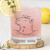 Capybara Rocks Glass filled with pink drink, garnished with a lemon slice and herb, showcasing detailed capybara illustration.