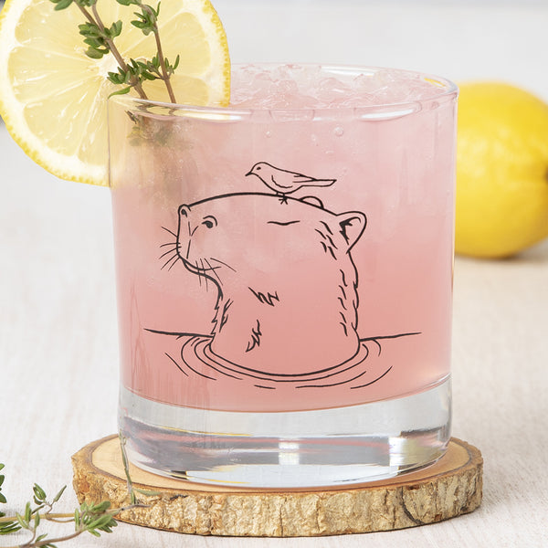 Capybara Rocks Glass filled with pink drink, garnished with a lemon slice and herb, showcasing detailed capybara illustration.