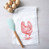 Counter Couture Chicken Flour Sack Towel featuring a hand-drawn chicken illustration, alongside a light blue silicone spatula and a carton of eggs on a wooden surface.