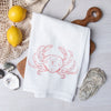 Dungeness Crab flour sack towel by Counter Couture, featuring a hand-drawn red crab illustration, styled in a kitchen setting with lemons and ocean-themed decor.