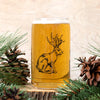 Visually similar image of Jackalope Beer Can Glass from Counter Couture, featuring a detailed jackalope illustration with beer inside, framed by pine foliage and cones.