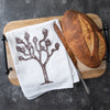 Counter Couture Joshua Tree flour sack towel displayed on a wooden cutting board with freshly baked bread.