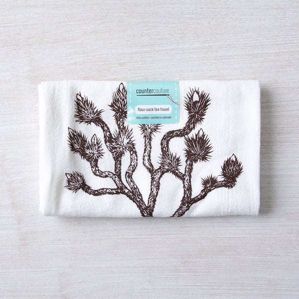 Counter Couture Joshua Tree flour sack towel wrapped with a label, placed on a light-colored wooden table.