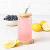 Refreshing pink drink in a mason jar topped with a bamboo lid and stainless steel straw, surrounded by lemon slices and blueberries from Counter Couture.