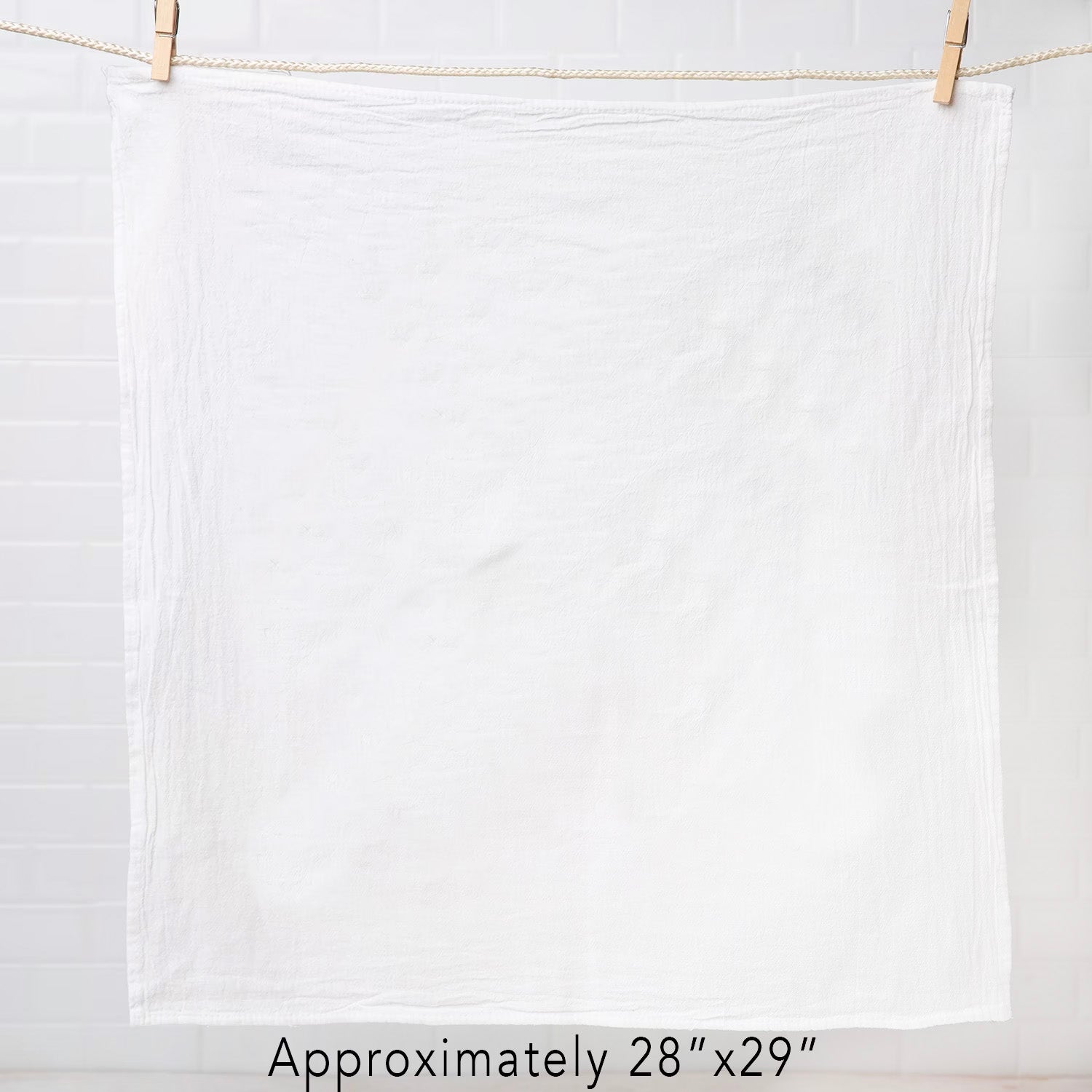 A white flour sack tea towel hanging with a clothespin, measuring approximately 28