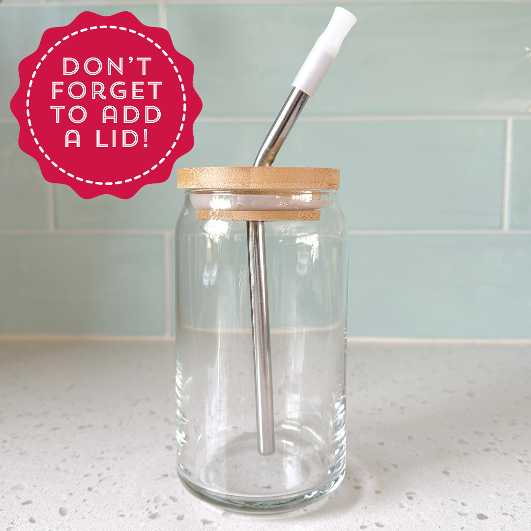 A clear glass jar with a bamboo lid and a metal straw inside, placed on a countertop. The image features a red circular note saying, 'Don’t forget to add a lid!' highlighting the jar's accessory.