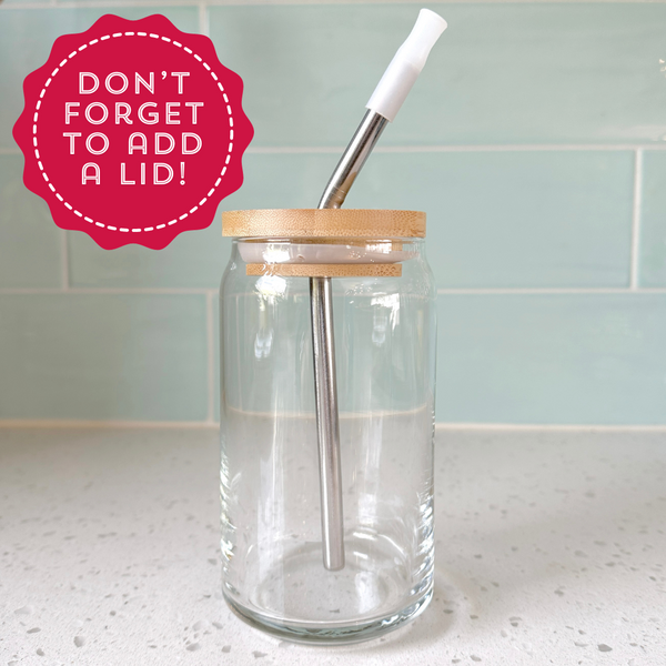 A clear glass jar with a bamboo lid and a metal straw inside, placed on a countertop. The image features a red circular note saying, 'Don’t forget to add a lid!' highlighting the jar's accessory.