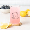 Another angle of the Capybara Beer Can Glass filled with a pink drink, highlighted by a whimsical capybara and bird illustration, with lemons and blueberries enhancing the presentation.