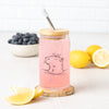 The Capybara Beer Can Glass topped with a bamboo lid and a straw, showcasing the same playful capybara design, surrounded by lemons and blueberries in the background.
