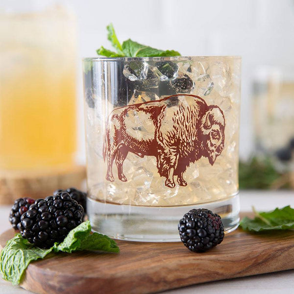 Bison rocks glass printed with a hand-drawn buffalo illustration, filled with an amber liquid, ice, and a mint garnish