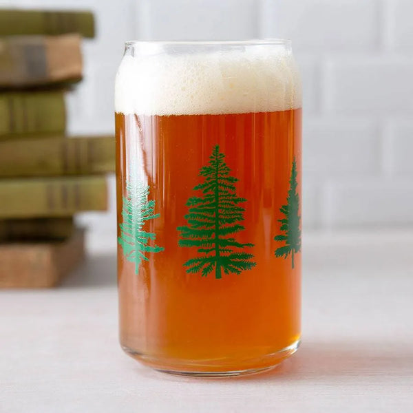 Beer glass with green tree design, filled with amber beer and foam, on a light surface
