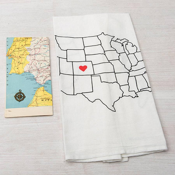 Flour sack tea towel with US map outline and red heart design, next to a vintage map on a light surface.