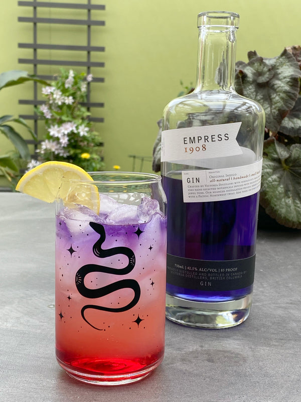 Snake design can-shaped glass with colorful gin cocktail, lemon slice garnish, Empress 1908 gin bottle