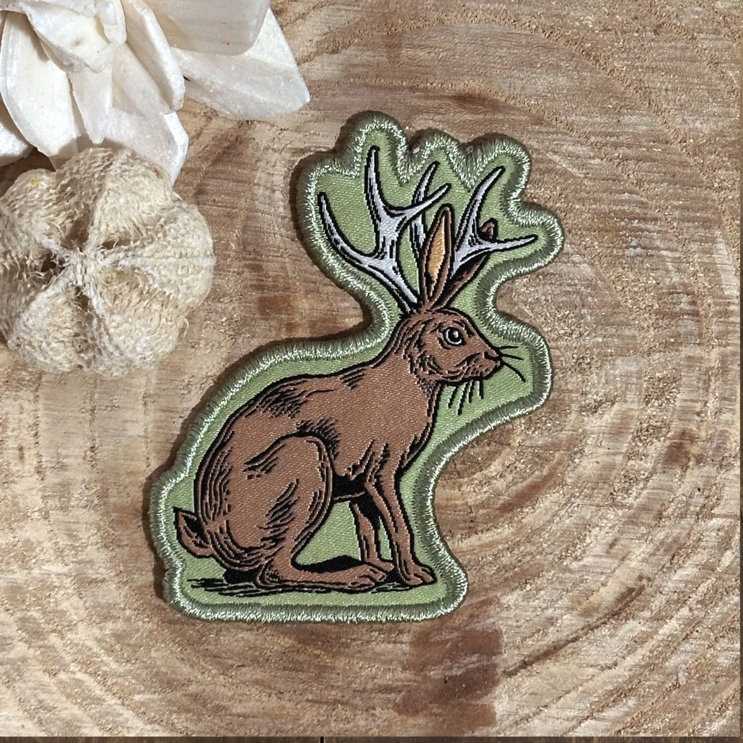 a patch depicting a brown rabbit with antlers, placed on a wooden surface.