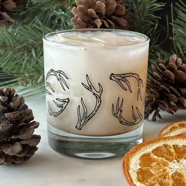 A rocks glass filled with a white drink and ice is printed with black hand-drawn antlers.