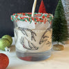 Festive rocks glass printed with antlers has green and red sprinkles around the rim and Christmas decor in the background.