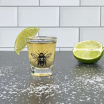 Bee shot glass with tequila, lime wedge, and salt on black counter with tile backdrop