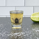Bee skull shot glass with yellow drink, lime wedge, and salt on black countertop