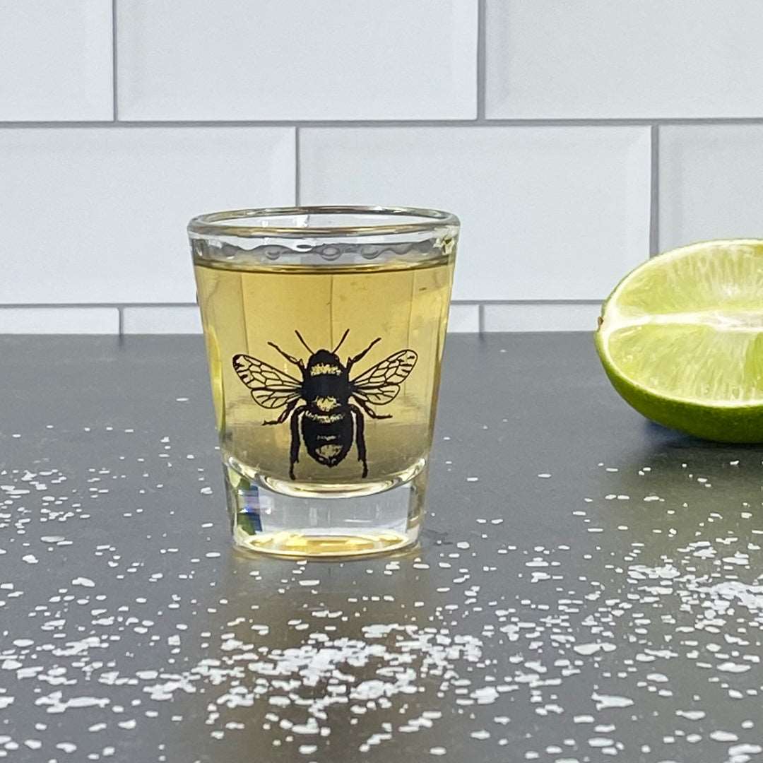 Bee skull shot glass with yellow drink, lime wedge, and salt on black countertop