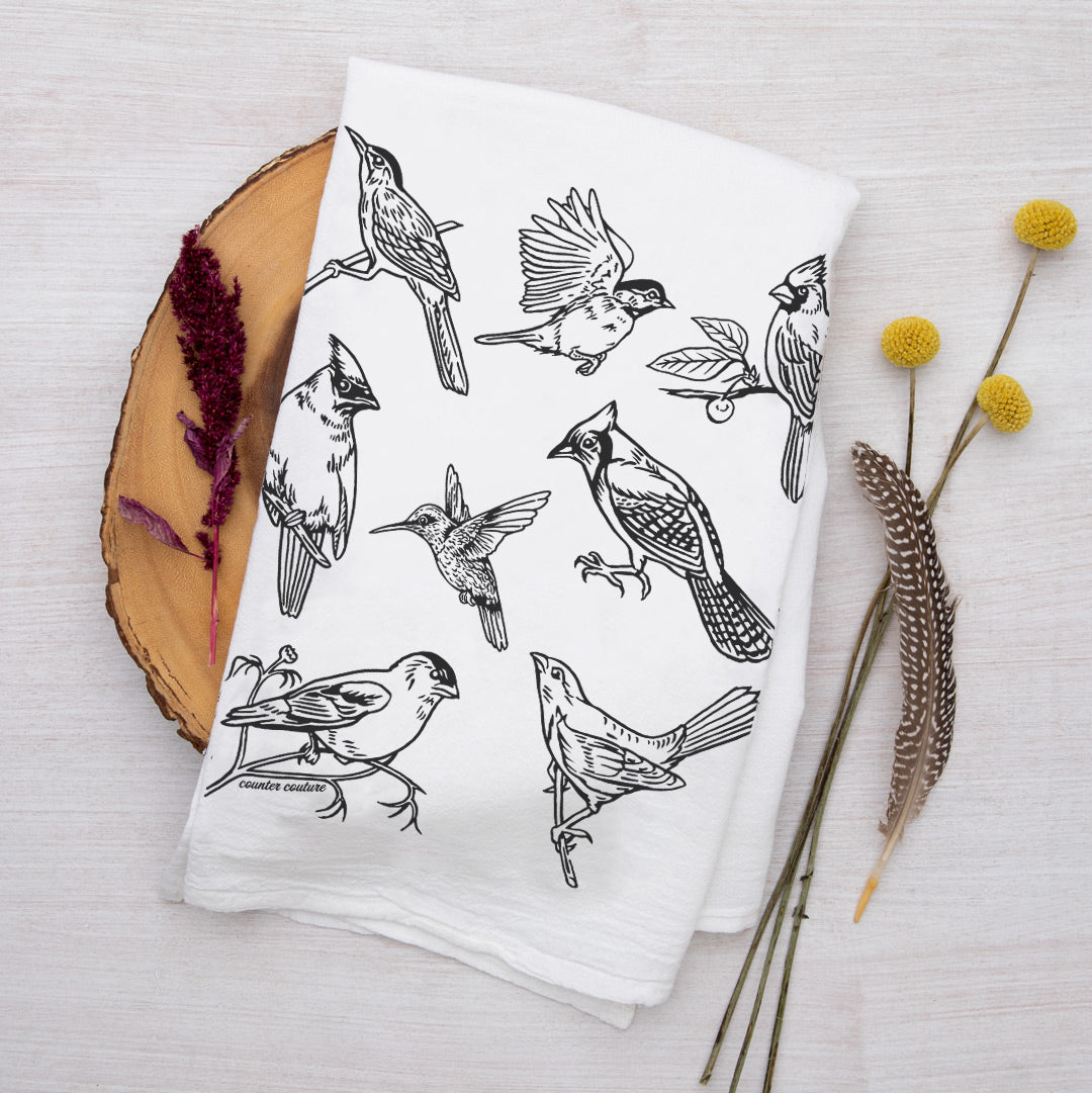 a white kitchen towel with a variety of black birds on it