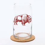Clear can-shaped beer glass with brown bison illustration, displayed on a cork coaster