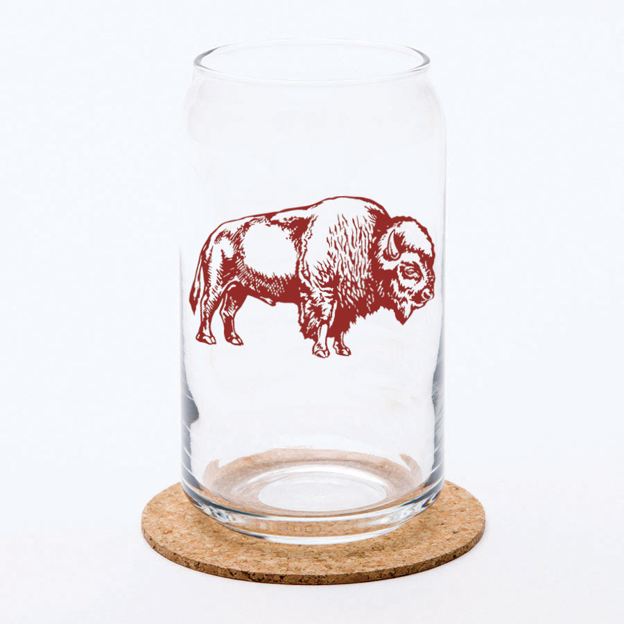 Clear can-shaped beer glass with brown bison illustration, displayed on a cork coaster