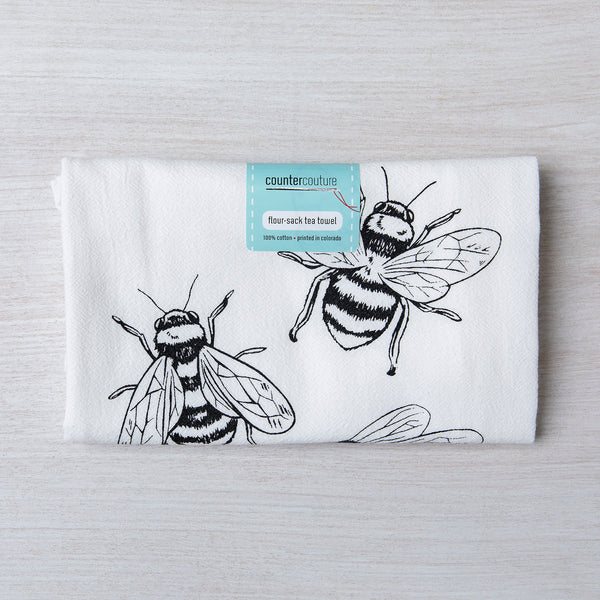 Folded Bumble Bee flour sack tea towel displaying intricate bee designs, with a tag indicating it is made of 100% cotton and printed in Colorado.