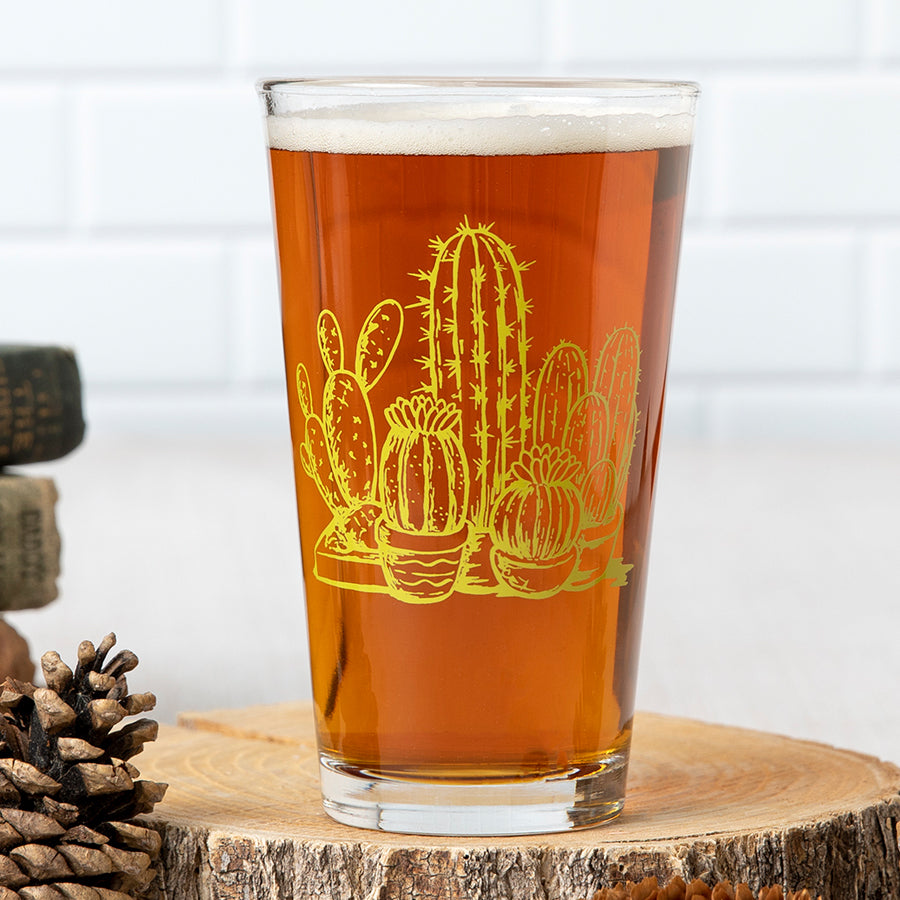 Pint glass with yellow cactus illustration, filled with beer, on a wooden coaster.