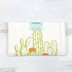 Flour sack tea towel with green cactus and orange flower print, folded on white background