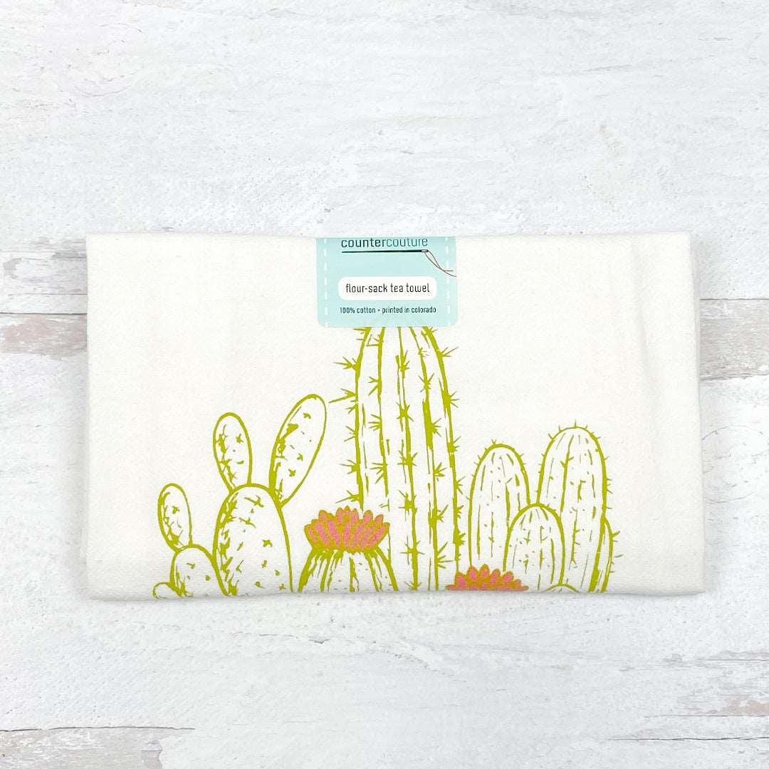 Flour sack tea towel with green cactus and orange flower print, folded on white background