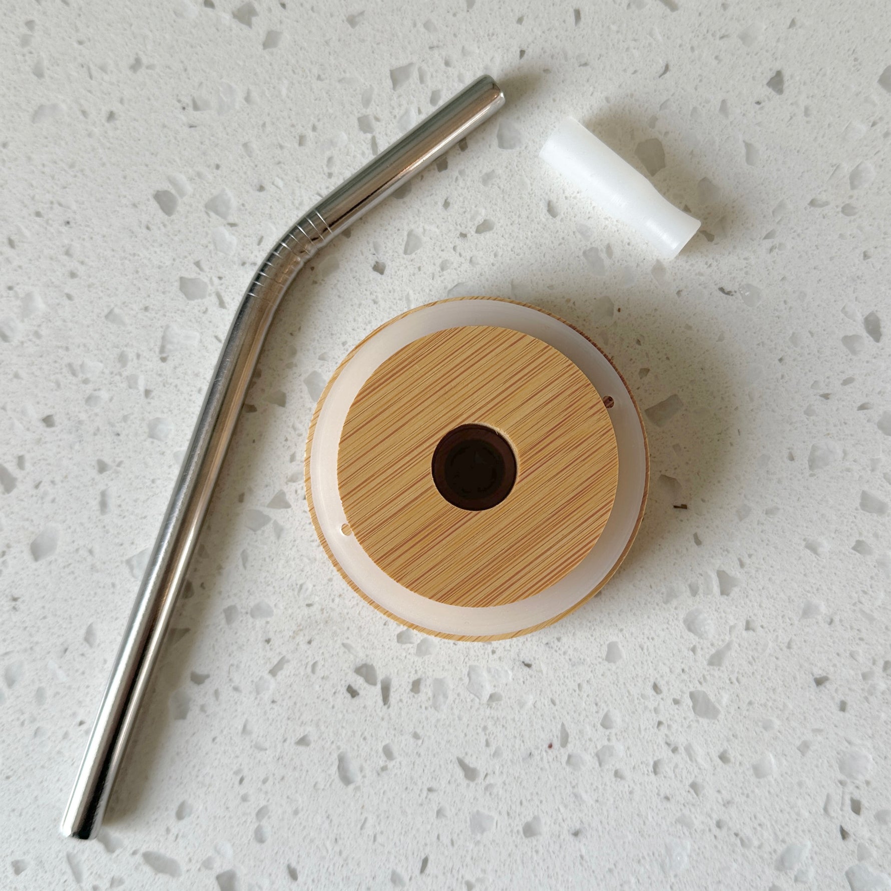 Bamboo lid, reusable metal straw, and silicone gasket on white countertop
