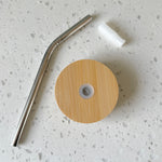 Bamboo glass lid, reusable metal straw, and silicone gasket on white countertop