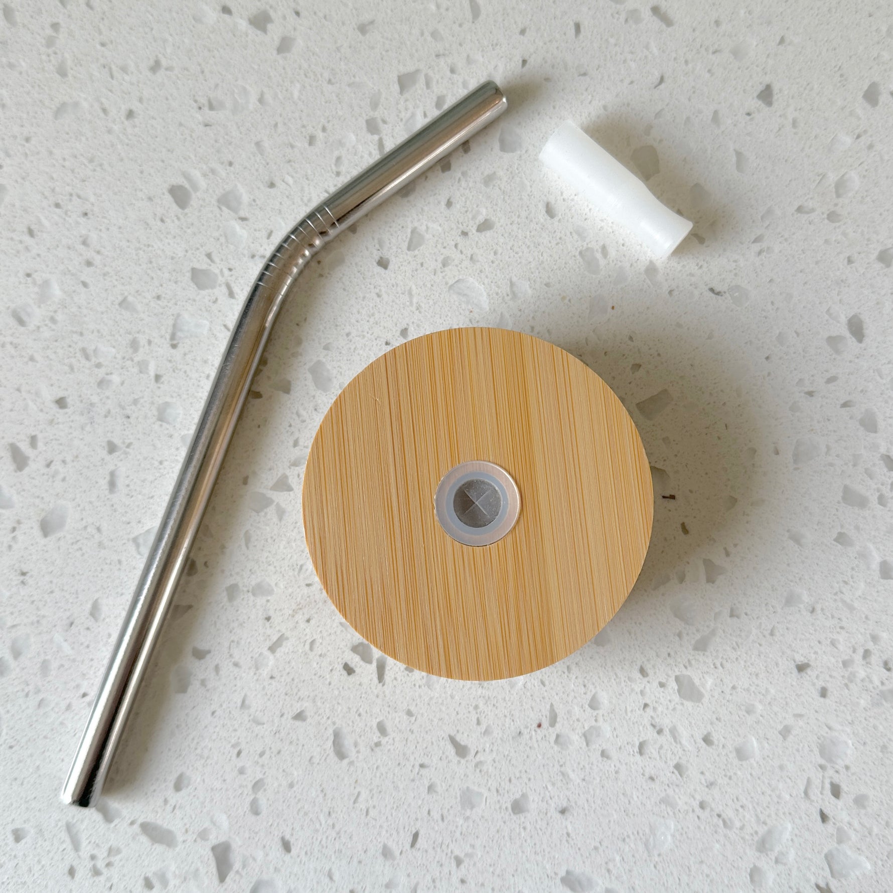 Bamboo glass lid, reusable metal straw, and silicone gasket on white countertop