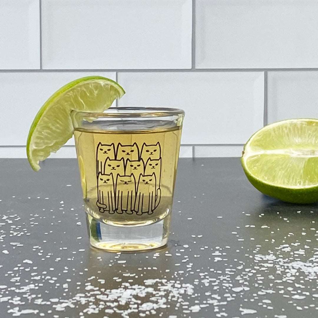 Cat illustration shot glass with tequila, lime wedge, and salt on a kitchen counter.