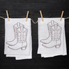 Set of two Cowboy Boot Tea Towels by Counter Couture hanging with clothespins, showcasing the hand-drawn cowboy boot design on a clean white fabric.