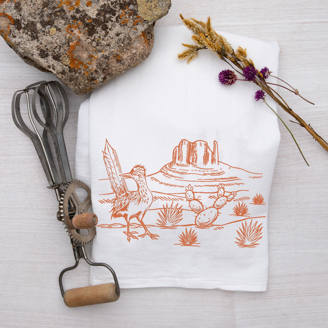 Desert-themed tea towel featuring a hand-drawn illustration of a bird and cactus against a scenic desert background. Created by Counter Couture, this eco-friendly cotton kitchen towel adds a rustic touch to any kitchen.