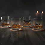 Set of four Halloween whiskey glasses with beetle, anatomical heart, moth and skull illustrations on a dark wood table