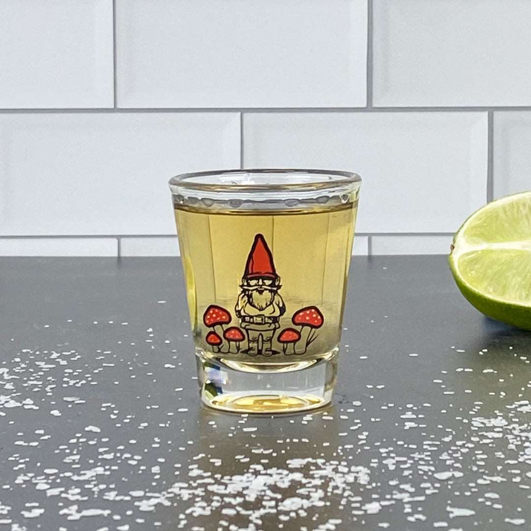 Gnome shot glass with red mushrooms, filled with liquor, lime and salt on black countertop