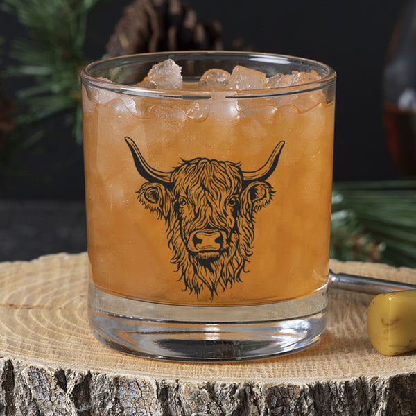 Chilled whiskey glass featuring a Highland cow illustration, perfect for serving cocktails, placed on a wooden slice.