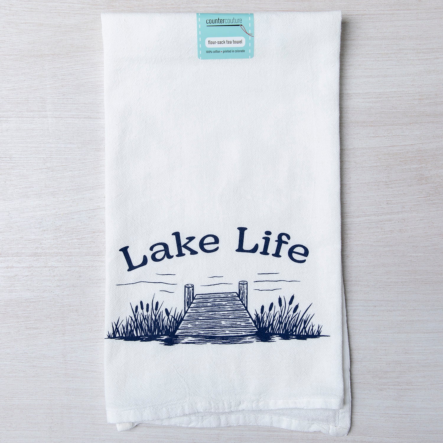 Counter Couture Lake Life flour sack towel showcasing a detailed print of a dock and grass with the words 'Lake Life', ideal for drying dishes in style.