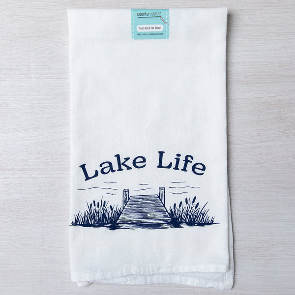 Counter Couture Lake Life flour sack towel showcasing a detailed print of a dock and grass with the words 'Lake Life', ideal for drying dishes in style.