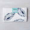 Folded oyster print flour sack tea towel by Counter Couture, showcasing detailed navy blue illustrations of oysters with a tag indicating material and design details.