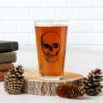 Pint glass with skull graphic filled with beer, on wood slice with pinecones, rustic decor