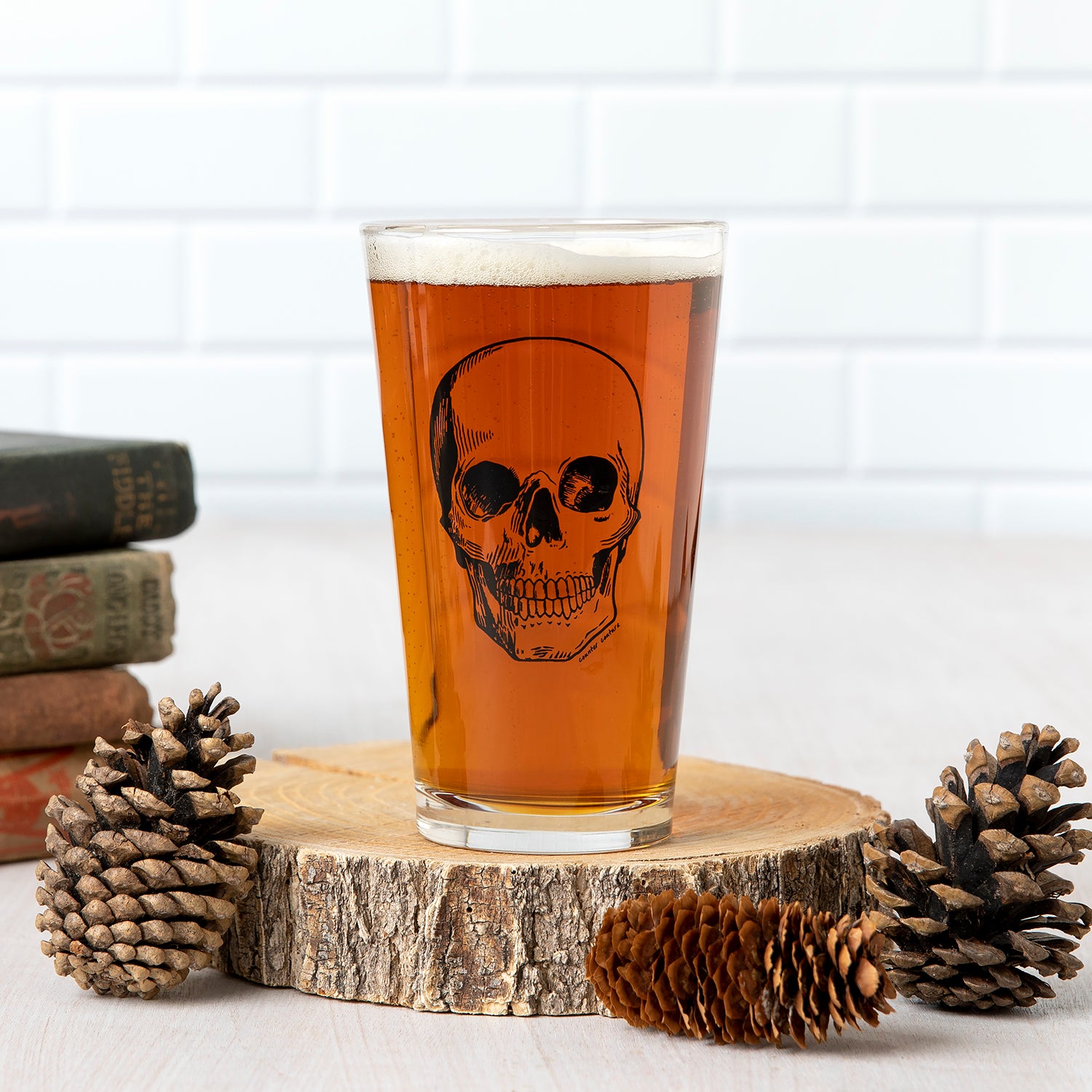 Pint glass with skull graphic filled with beer, on wood slice with pinecones, rustic decor