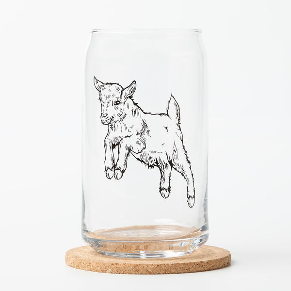 Clear Beer Can Glass showcasing a black outline illustration of a leaping baby goat, resting on a cork coaster against a clean white background. The design highlights the unique shape of the glass.