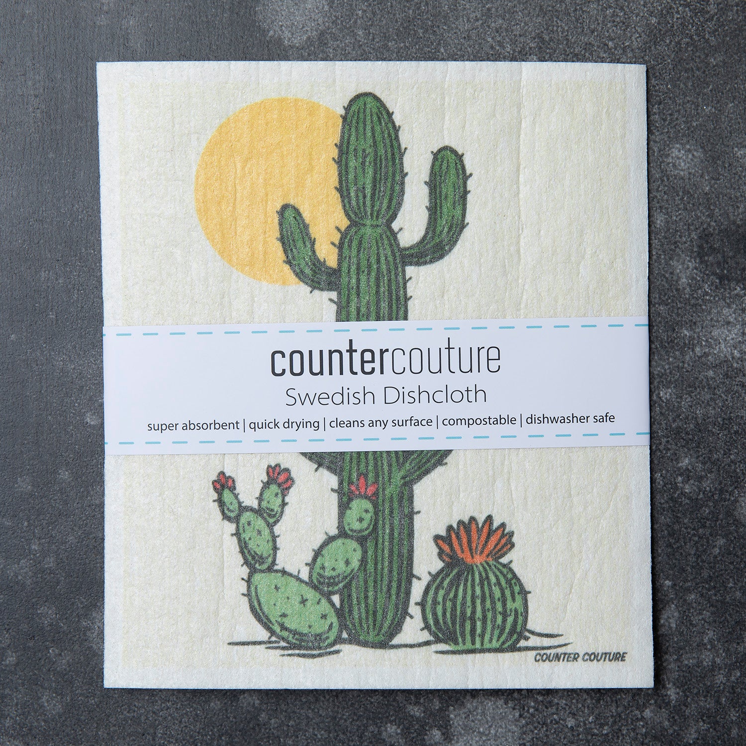 Counter Couture Swedish Dishcloth showcasing a design of a saguaro cactus and two smaller cacti with a yellow sun. The dishcloth is packaged with information about its absorbency and eco-friendly features.
