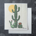 Saguaro Cactus Swedish Dishcloth by Counter Couture featuring a tall saguaro cactus alongside two smaller cacti and a sun in the background. Perfect for versatile cleaning tasks.