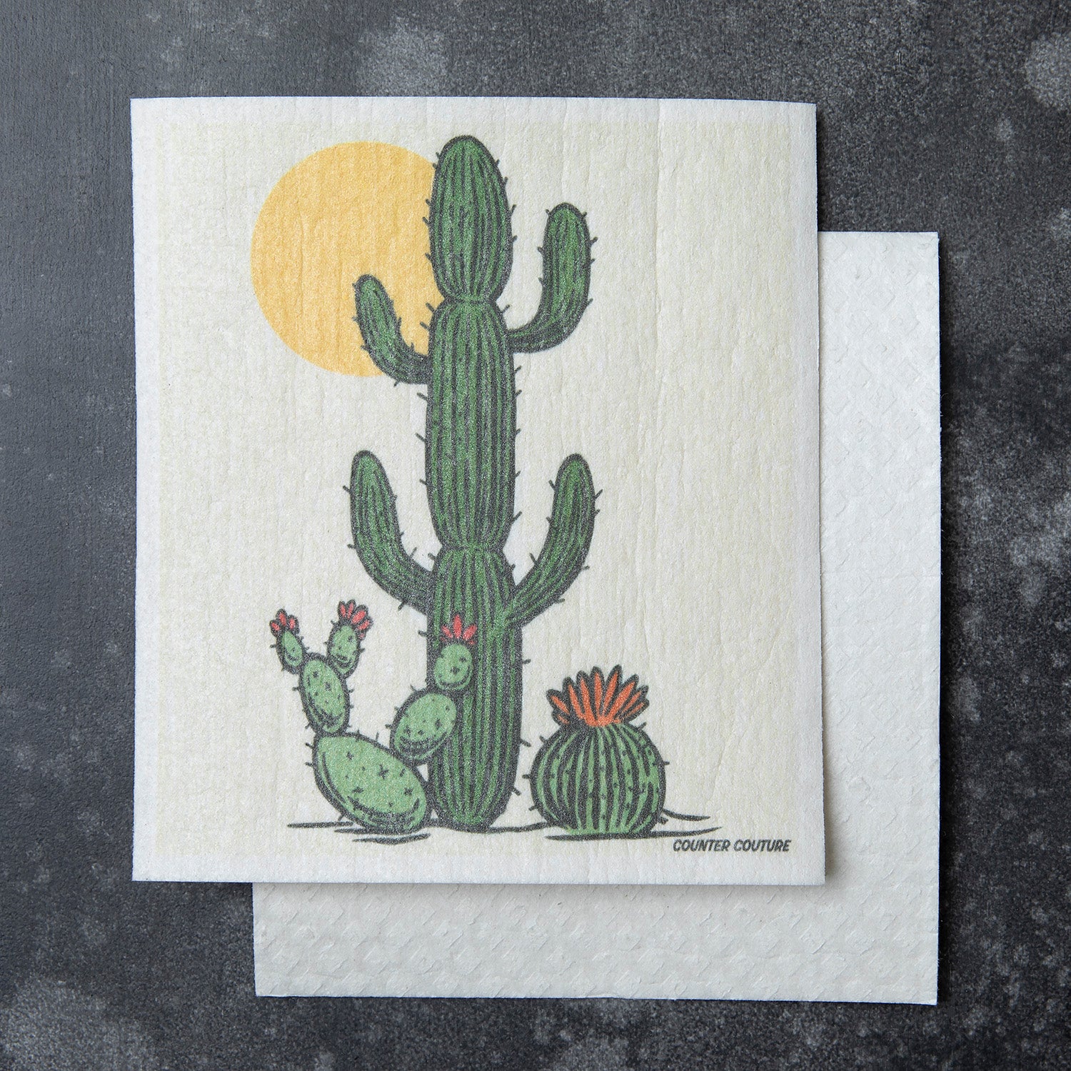 Saguaro Cactus Swedish Dishcloth by Counter Couture featuring a tall saguaro cactus alongside two smaller cacti and a sun in the background. Perfect for versatile cleaning tasks.